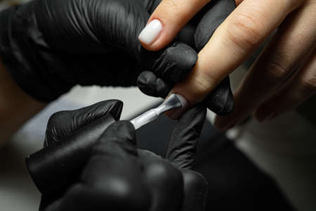 the process of applying varnish on nails in a beauty salon close-up. A woman in the salon receives a manicure from a beautician. Transparent nail polish and brush, macro. Shallow depth of fieldの写真素材