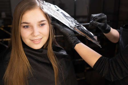 The hairdresser dyes women's hair, highlighting the hair of his client with a brush and foil. selective focus.の写真素材