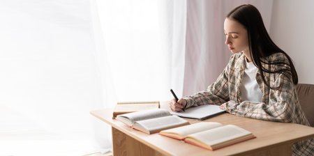 Purposeful female student studying with writing reference book, doing homework, concentrated teenage...