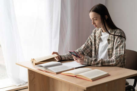 college girl student studying remotely using modern smartphone, distance education lesson online at home, technology for e-learning, profile view, education conceptの写真素材