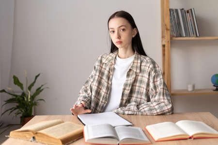education concept, high school student sitting at a desk at home with books, young girl studying at home, searching for information for an examの写真素材