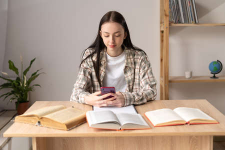 Girl student studying online using smartphone, education with mobile phone, distance learning, gadget user on webinar, study at home, homework e-learningの写真素材