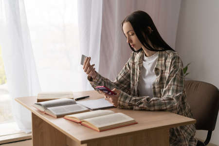 cashless payment system concept, young caucasian student girl shopping online using credit card and smartphone, online payments at homeの写真素材
