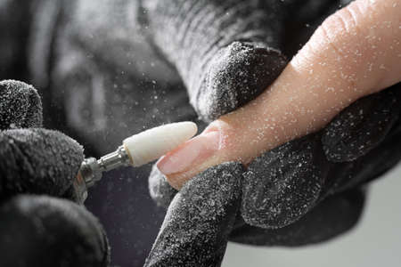 Manicurist uses an electric drill to remove old gel polish from nails. A woman is getting a manicure of nails. The beautician files the client's nails. professional manicure tool. close-upの写真素材