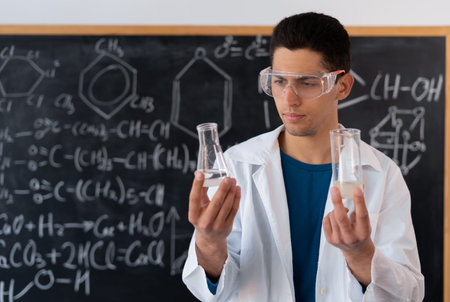 A young Arab male chemistry teacher stands against the background of a chalk board with different...