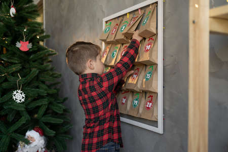 child boy taking a gift, handmade advent calendar day from craft bags with sweets. Eco friendly Christmas, zero waste, childrens seasonal activities, Christmas traditionの写真素材