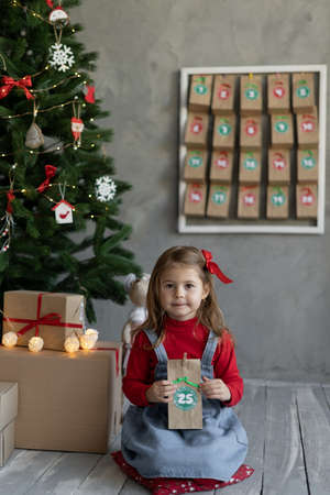 Child with handmade advent calendar gift in the room, Christmas children fan, winter traditions, gift package with candiesの写真素材