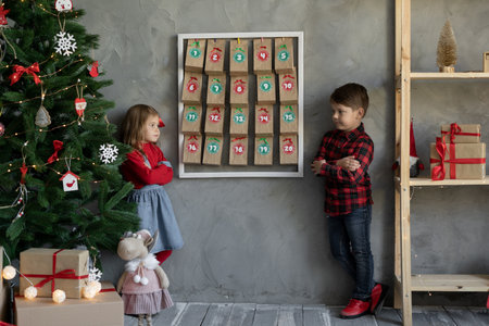 Portrait of little brother and sister on handmade advent calendar background, kids in room with christmas decor, children christmas fanの写真素材