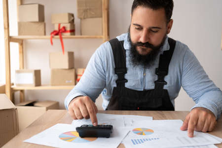 Close-up, Indian business man calculating with machine, managing finance risks at home, focused bi-racial man doing calculations on calculator, paying bills, taxes or expenses, man analysis in officeの写真素材
