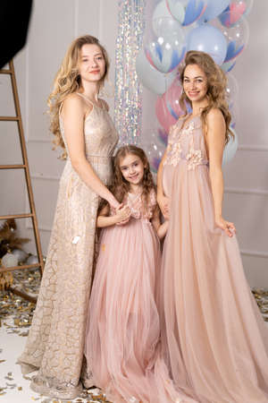 Charming laughing birthday girl with colorful balloons hugging her young smiling mom and girlfriend after a funny event. Attractive women posing with beautiful daughter at a partyの写真素材