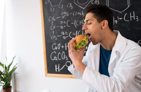 asian worker of food control eating hamburger by workplace while checking quality and taste of its...