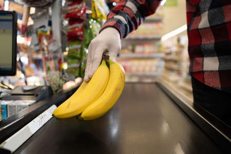 close up young man putting goods on counter in supermarket, bunch of bananas at store checkout, shoppingの写真素材