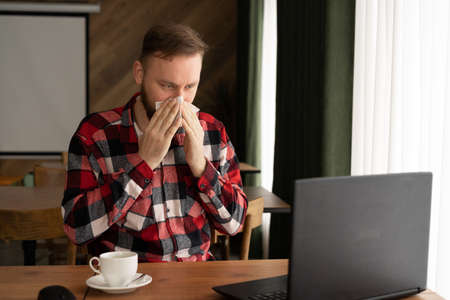 selective focus of businessman sneezing in tissue while looking at laptop in home office or cafe, freelancer allergic or fluの写真素材