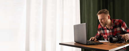 Photographer off loading files on laptop. Checking photos working at modern office. editing his images on laptop. bannerの写真素材