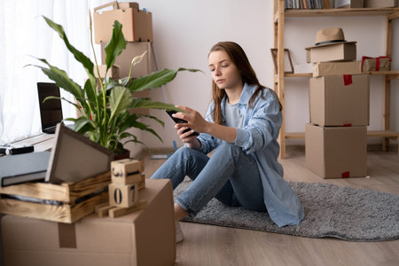 Moving day. Home move out of apartment moving boxes woman using online movers services on mobile...