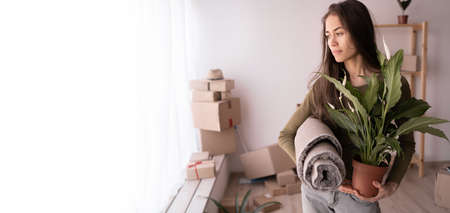 young hispanic woman moves with her favorite plant to a new house, relocation to purchased apartments, owner of a new home, concept of moving and relocation, bannerの写真素材