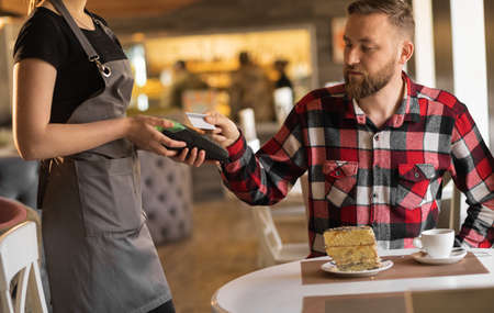 caucasian man paying through payment terminal in hands of waitress, paying with credit card in cafe, customer making contactless payment with debit cardの写真素材