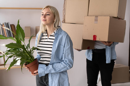 caucasian couple moving to new apartment, standing together over wall with big paper boxes full of...
