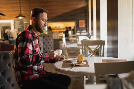 side view of young man having cup of coffee and eating pastry in a cafeの写真素材