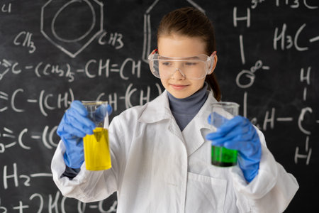funny scientist child with goggles in lab coat with chemical flasks, blackboard background with science formulas in the laboratory, back to school conceptの写真素材