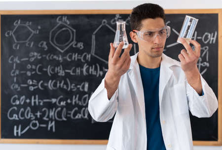 muslim young chemist conducting experiment mixing liquids in flask, laboratory assistant in goggles showing chemical reaction, science conceptの写真素材