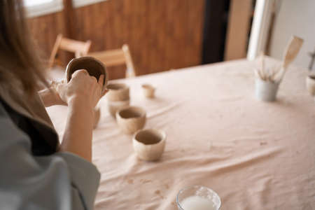 Potter at work. Potters hands in clay form a pot in a circle. close-up of female sculpting bowls from raw wet clay.の写真素材