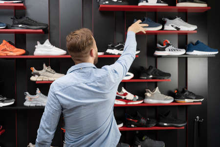 young man picking a sporty shoes in the shop, new sneakers in sports store for men, shopping sports shoesの写真素材