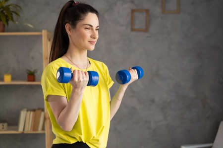 woman losing weight at home and exercising with dumbbells. Beautiful latin girl in sportswear with dumbbells in her hands. pumping up muscles biceps, concept fitness sport trainingの写真素材