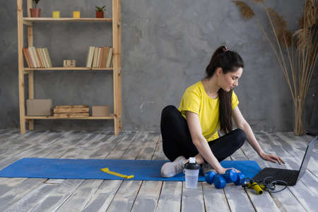 Attractive young woman doing yoga stretching online using a laptop at home. entertainment and education on the Internet. Sport and healthy lifestyleの写真素材