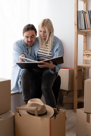 Cute couple unpacking cardboard boxes in new home, sitting on the floor and looking at a family...