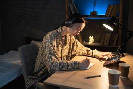 Asian girl is studying online with tablet at desk at night, online learning at homeの写真素材