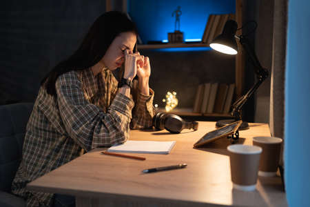 Fatigued asian woman student suffering eyestrain using tablet pc complaining at night at home. tired stressed young college girl massage nose bridge while painful.の写真素材