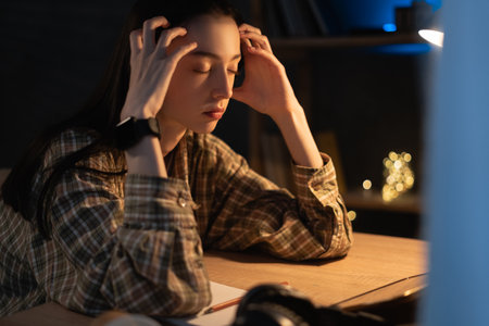 Female student studying at home getting headache at night. Tired girl and college education feel stressful. mixed race asian chineseの写真素材