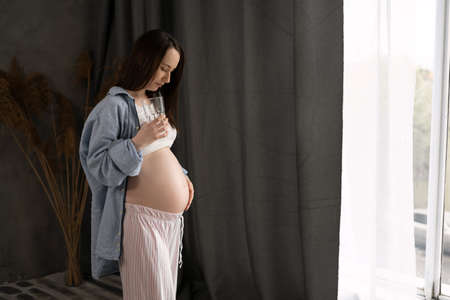 pregnant woman drinking pure water from a glass at home, expectant mother takes care of babys healthの写真素材