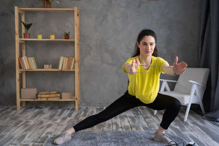 Young latin woman exercising at home, stretching legs and arms. Workout with resistance band on grey background. sport, athletics and healthy lifestyleの写真素材