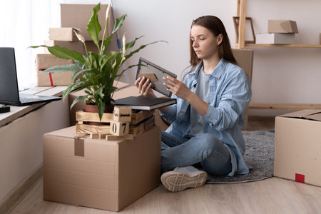 Young woman moving to new place sitting on floor hugging holding frame looking at photo cheerfulの写真素材