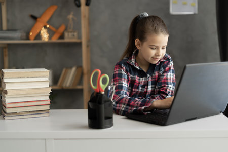 Schoolgirl studying at home using laptop. Girl pupill teaches a lesson online using a pc video chat call conference with a teacher at home. Homeschooling, online education, e-learningの写真素材