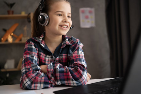 happy smiling teenage student girl in headphones with laptop computer at home. online lesson video call sit desk use earphones. children, education and distant learningの写真素材