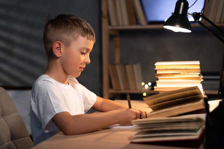 young teenager schoolboy at the table doing homework at home in eveningの写真素材