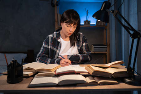 Female student reading book, prepare for exam at table at night. Educationの写真素材