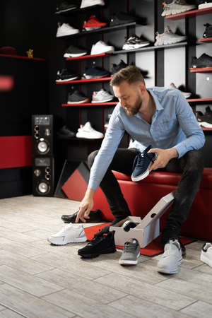 Young man choosing sneakers at sportswear shop, male shoe shopperの写真素材