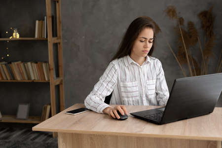 pretty brunette woman typing email on laptop computer while sitting working at home officeの写真素材