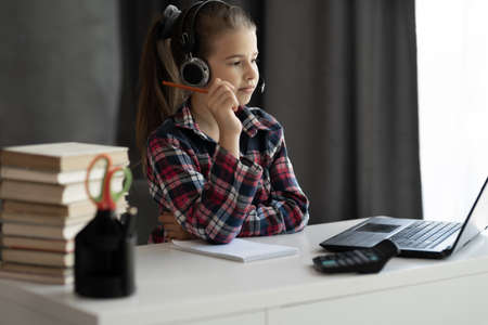 Portrait of student learning online with headphones and laptop taking notes while sitting at her desk at home. study remote use laptop online teacher communication chatting. Home schoolingの写真素材