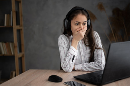 Young female watching scary movie, hiding face in fear, online film service. Hispanic young woman in headphones watching drama movie, worrying for charactersの写真素材