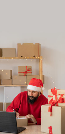 Indian bearded man wearing a Santa Claus hat works in a warehouse of boxes with gifts and orders...