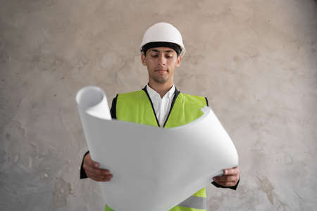 Young muslim architect man wearing contractor helmet holding project blueprints paper plan over isolated background construction, happy with big smile. White Hard Helmet. cの写真素材