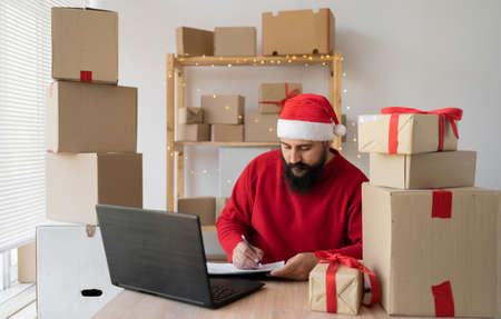 Indian Santa small and medium business freelance working in home office using computer, online marketing packaging box and gifts for Christmas delivery, SME e-commerce telemarketingの写真素材