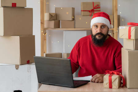 small business owner Indian freelance Santa working in home office using computer, online marketing packaging box and gifts for Christmas delivery, SME e-commerceの写真素材