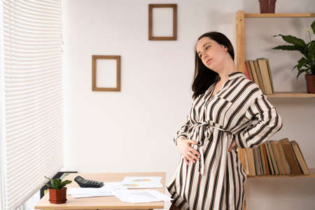 pregnant businesswoman working at home office with papers documents, resting with back pain. business and pregnancyの写真素材