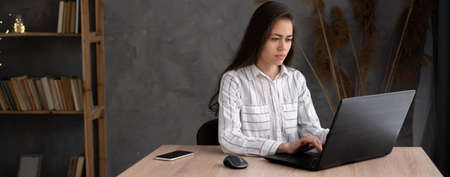 Serious young woman freelancer working on computer at home. Attractive businesswoman studying online, using laptop, web surfing information or shopping in internet store. bannerの写真素材